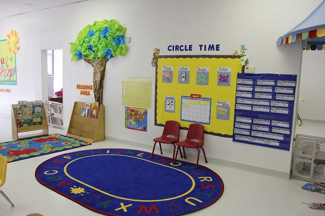 Classroom with a blue oval rug, two red chairs, and a yellow bulletin board