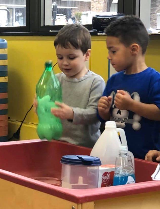 Two children playing with a green bottle over a red bin