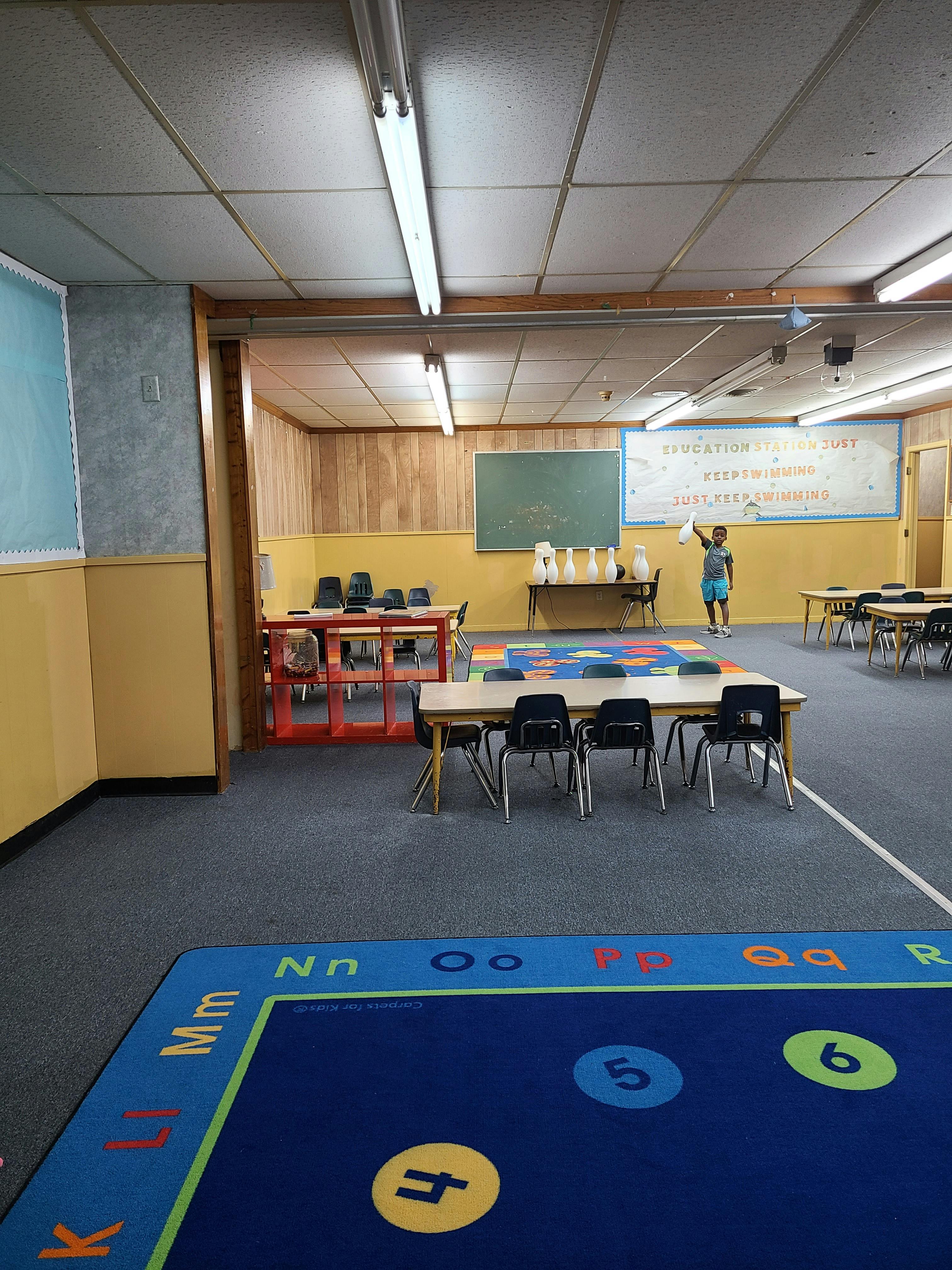 Classroom with tables, chairs, and a person standing near a chalkboard