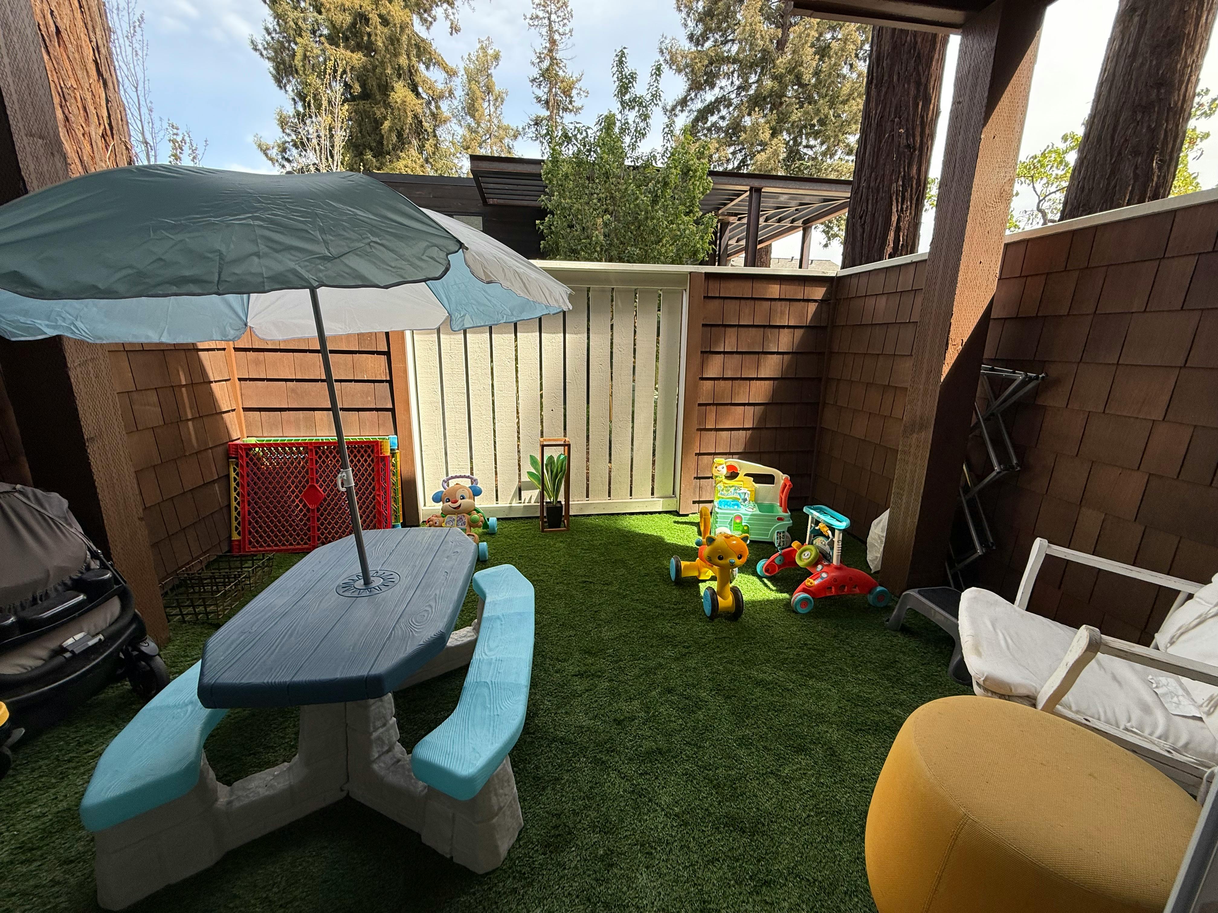 Outdoor play area with a small picnic table and various toys on artificial grass