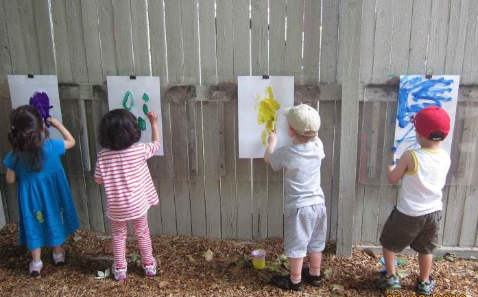 Four children painting on paper attached to a fence
