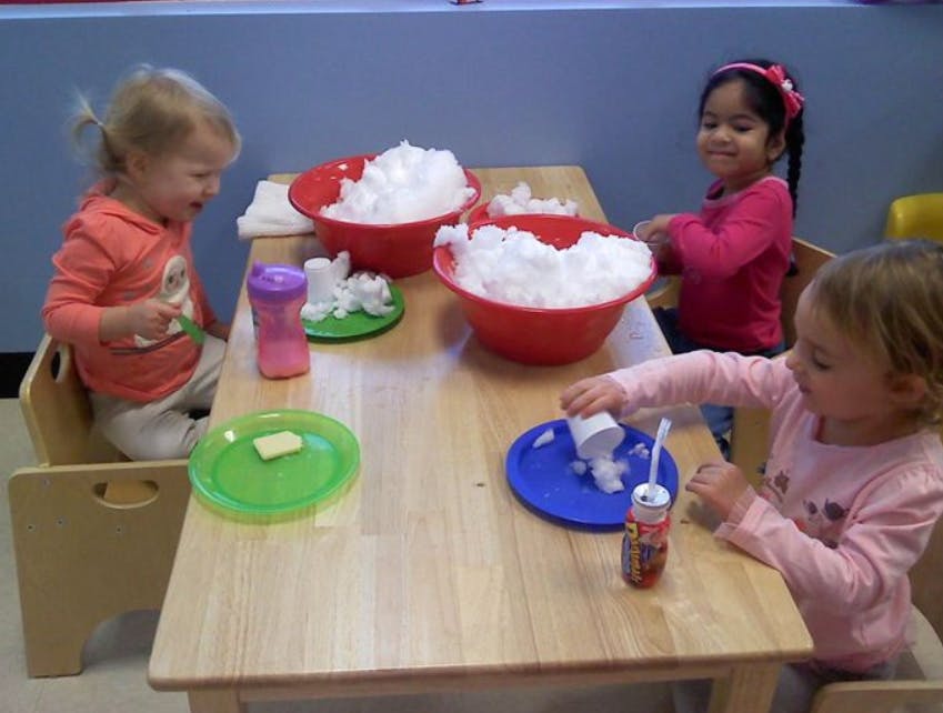 Three children at a table playing with bowls of white material