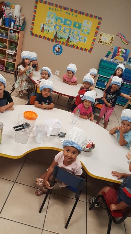 Children wearing chef hats sitting at tables in a classroom
