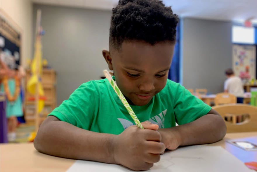 Child writing with a pencil in a classroom