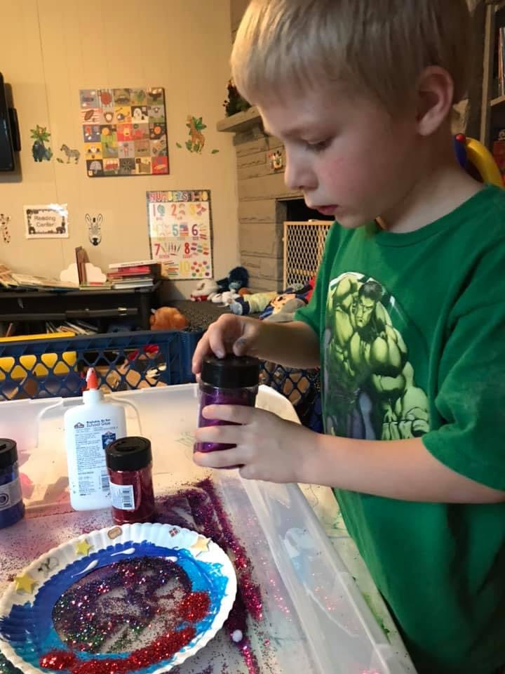 Child holding a container of glitter over a craft project