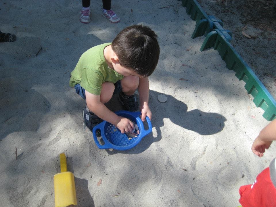 Child playing in sand with a blue toy