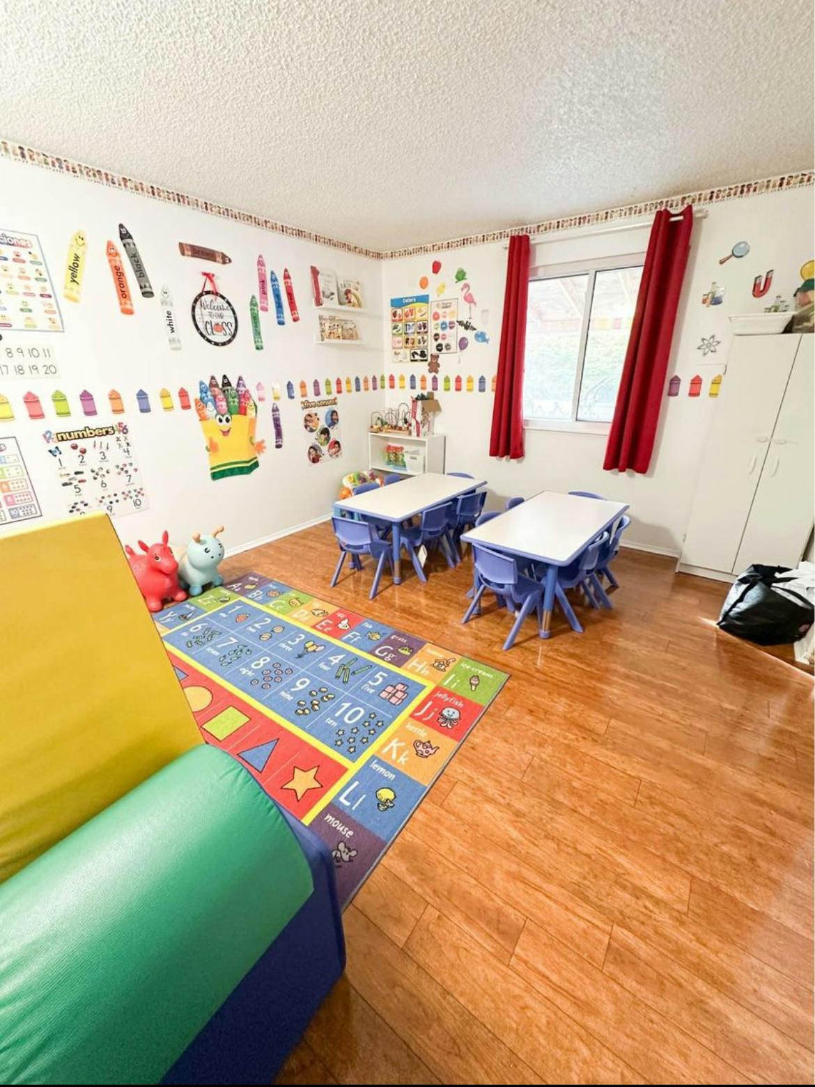 Classroom with small tables and chairs, colorful rug, and wall decorations