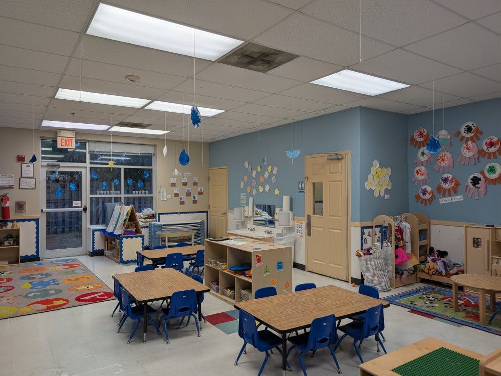 Empty classroom with small tables and chairs, and children's art on the walls