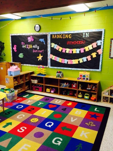 Classroom with a colorful alphabet rug, shelves with toys, and bulletin boards