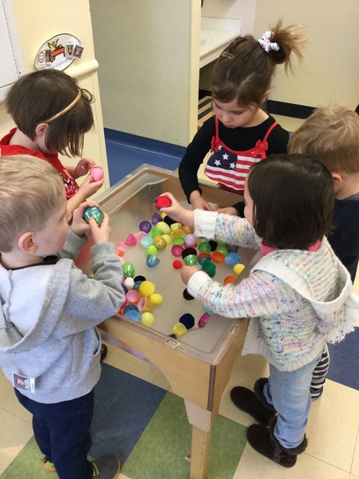 Children playing with colorful plastic eggs in a sand and water table