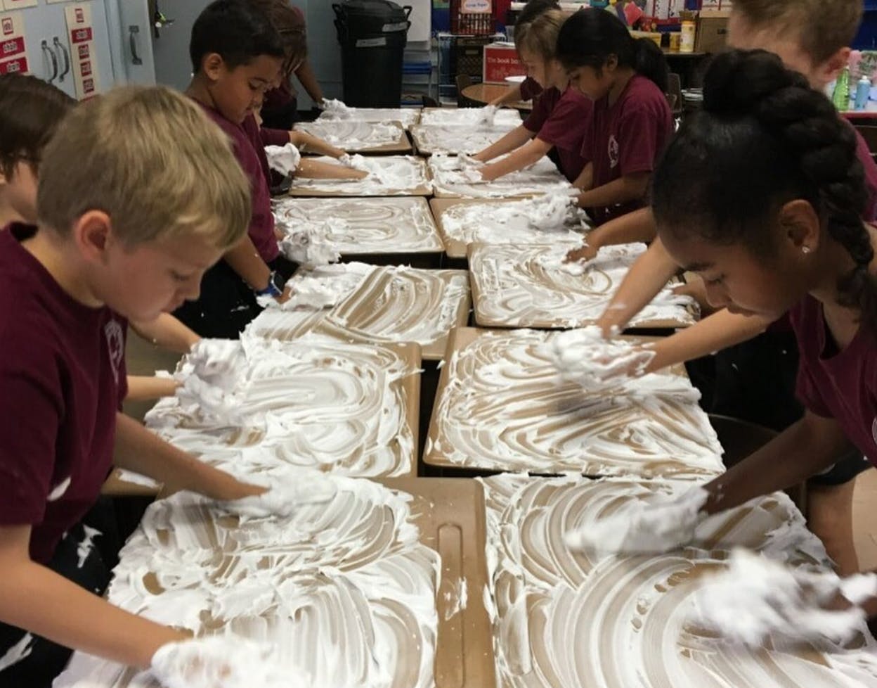Children playing with shaving cream on cardboard squares of cardboard squares