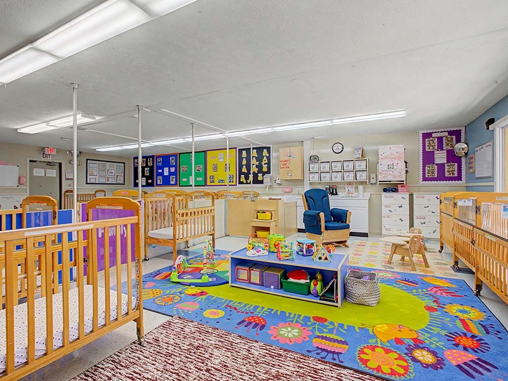 cribs in a bright nursery room with a colorful play rug