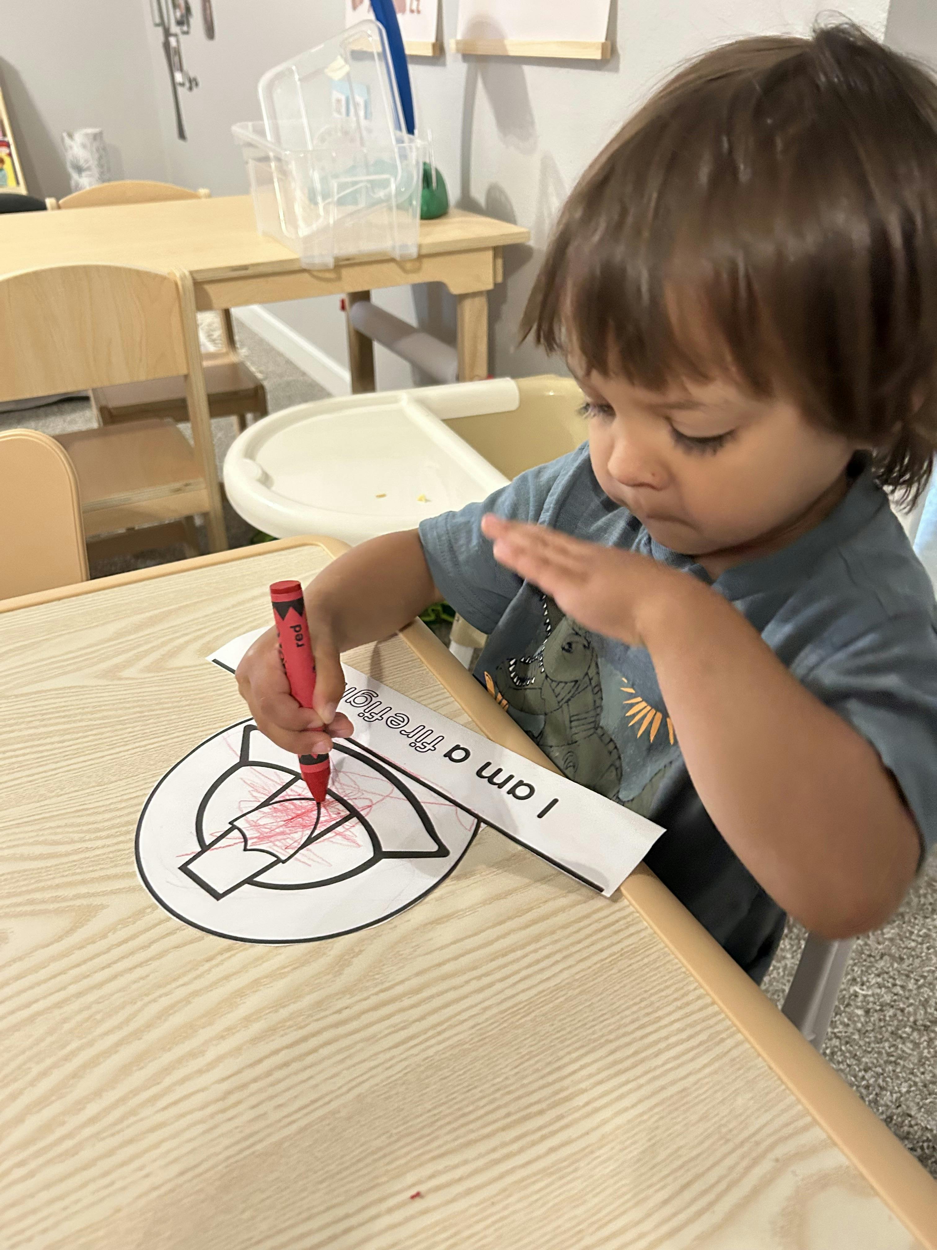 Child coloring a drawing with a red crayon