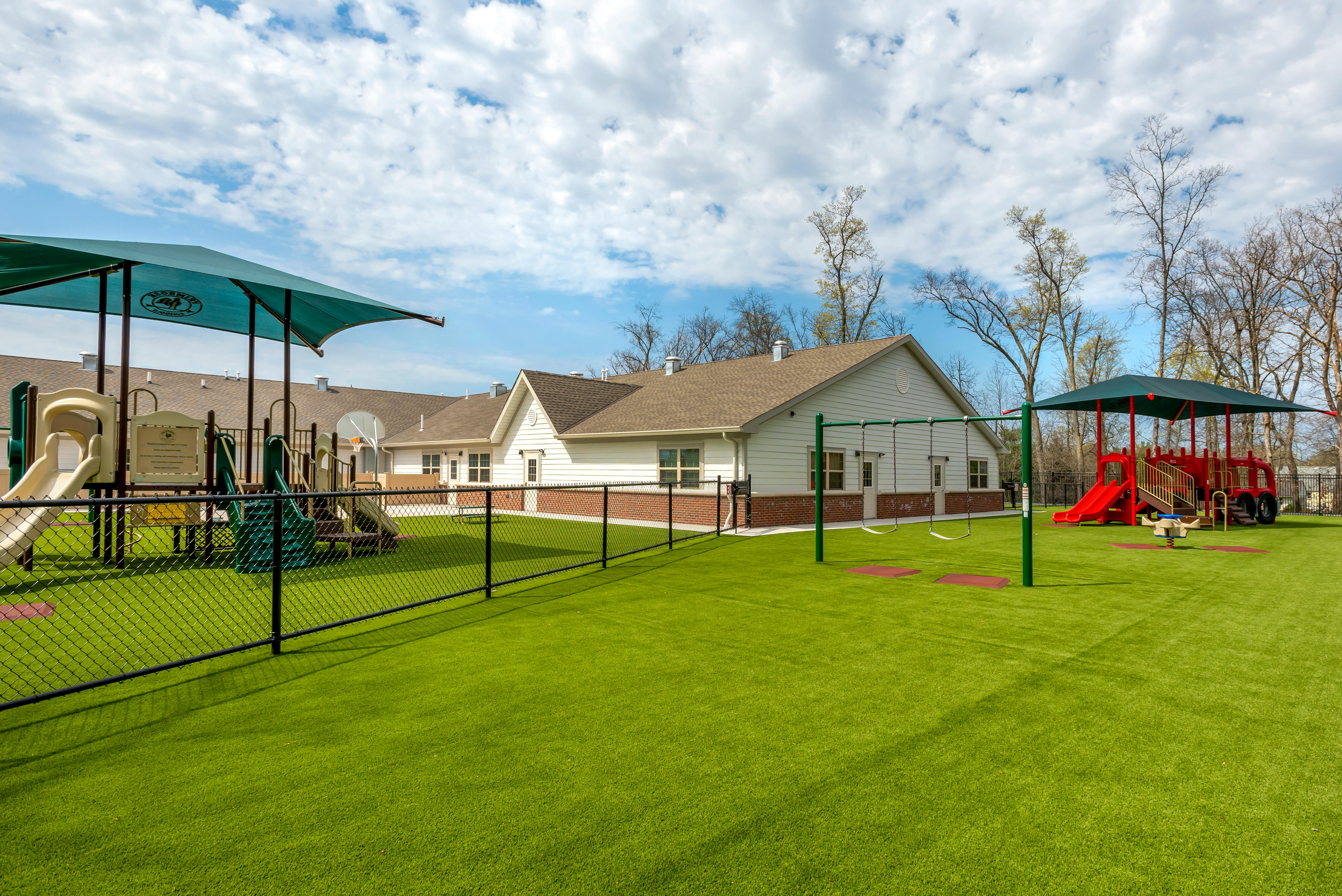 Fenced playground area with slides, swings, and a spring rider on artificial turf
