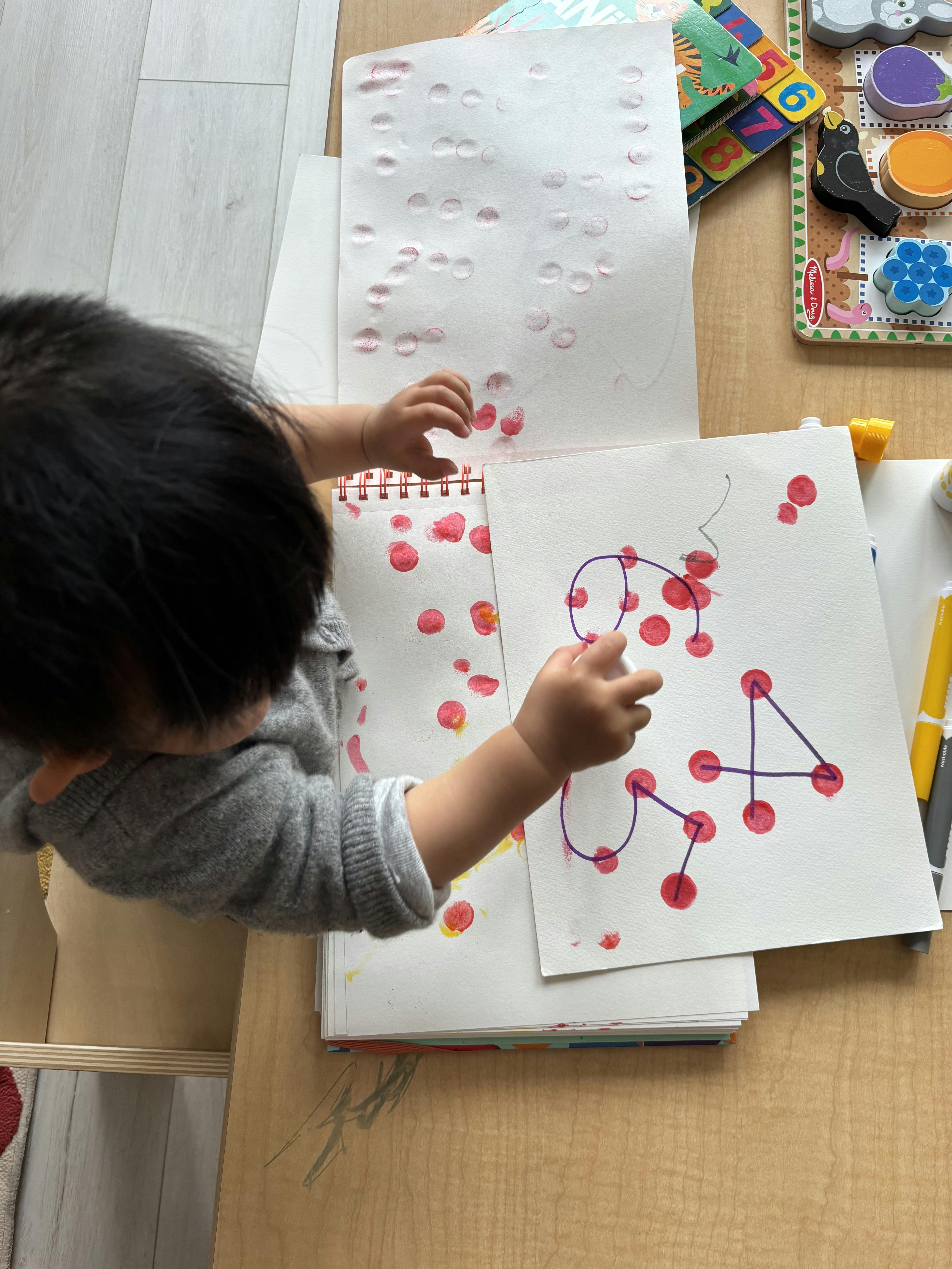 Child drawing on paper with red dots and purple lines