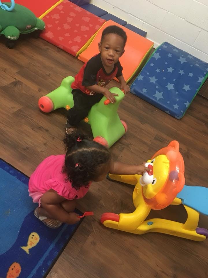Child on a green ride-on toy, another child playing with a lion toy