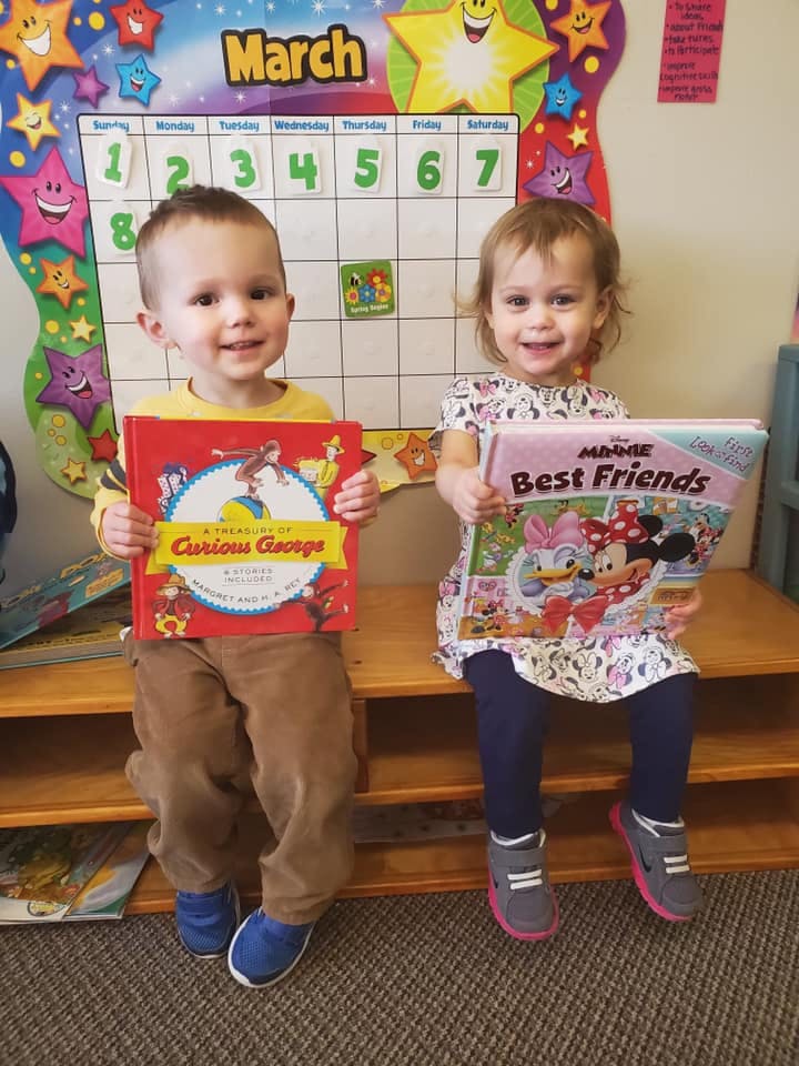 Two children sitting on a bench holding books in front of a calendar