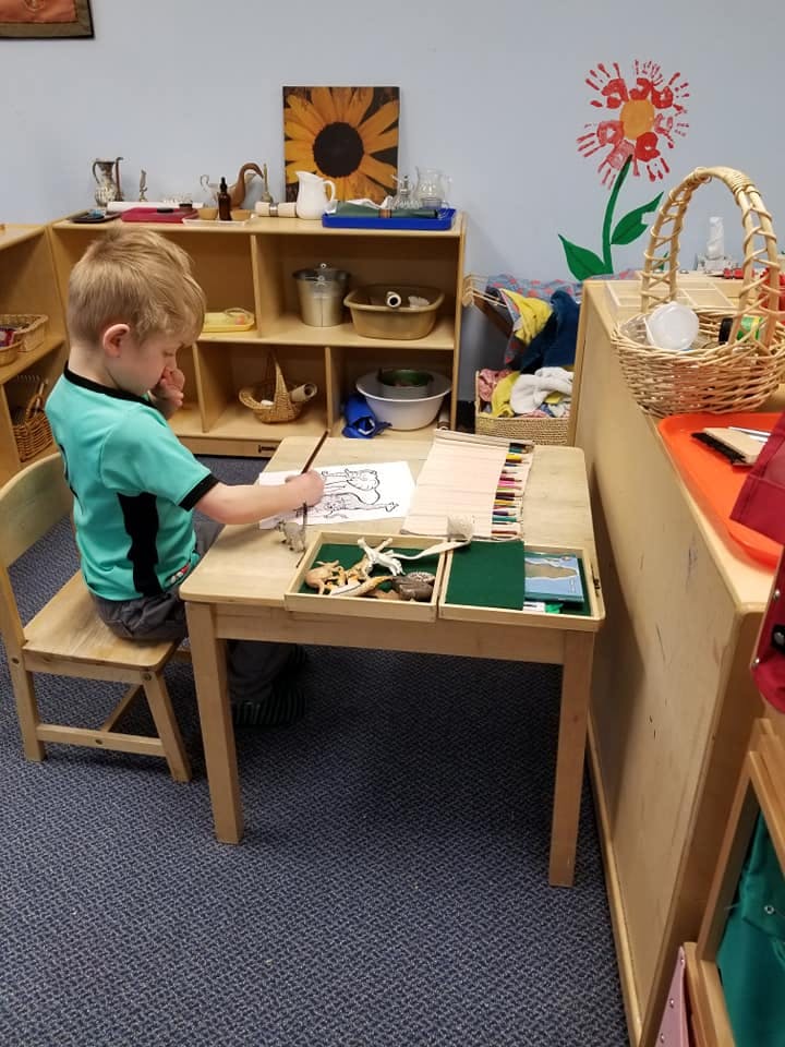 Child sitting at a small table drawing on paper