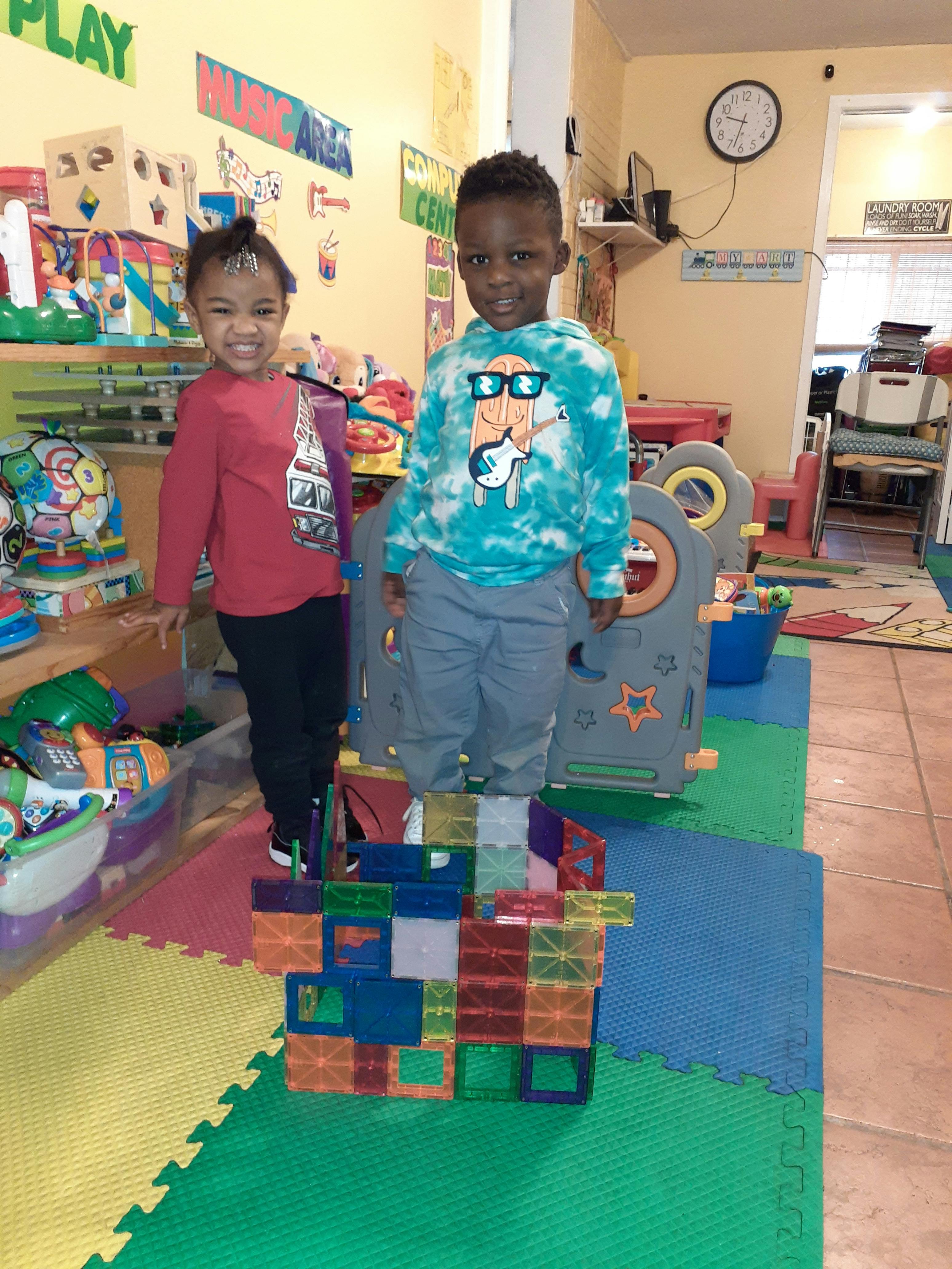 Two children standing in a classroom, one on a block structure