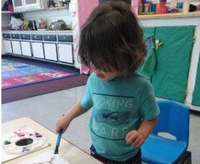 Child painting at a table in a classroom