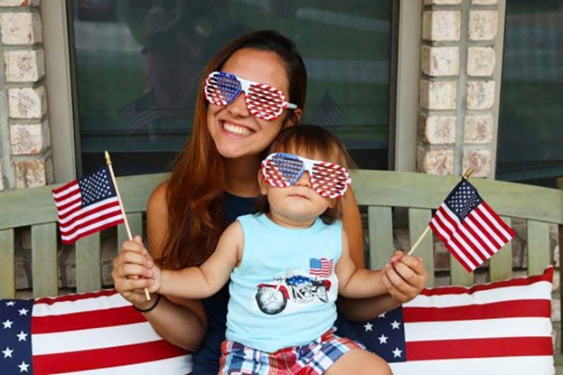 Person and child wearing patriotic sunglasses, holding American flags