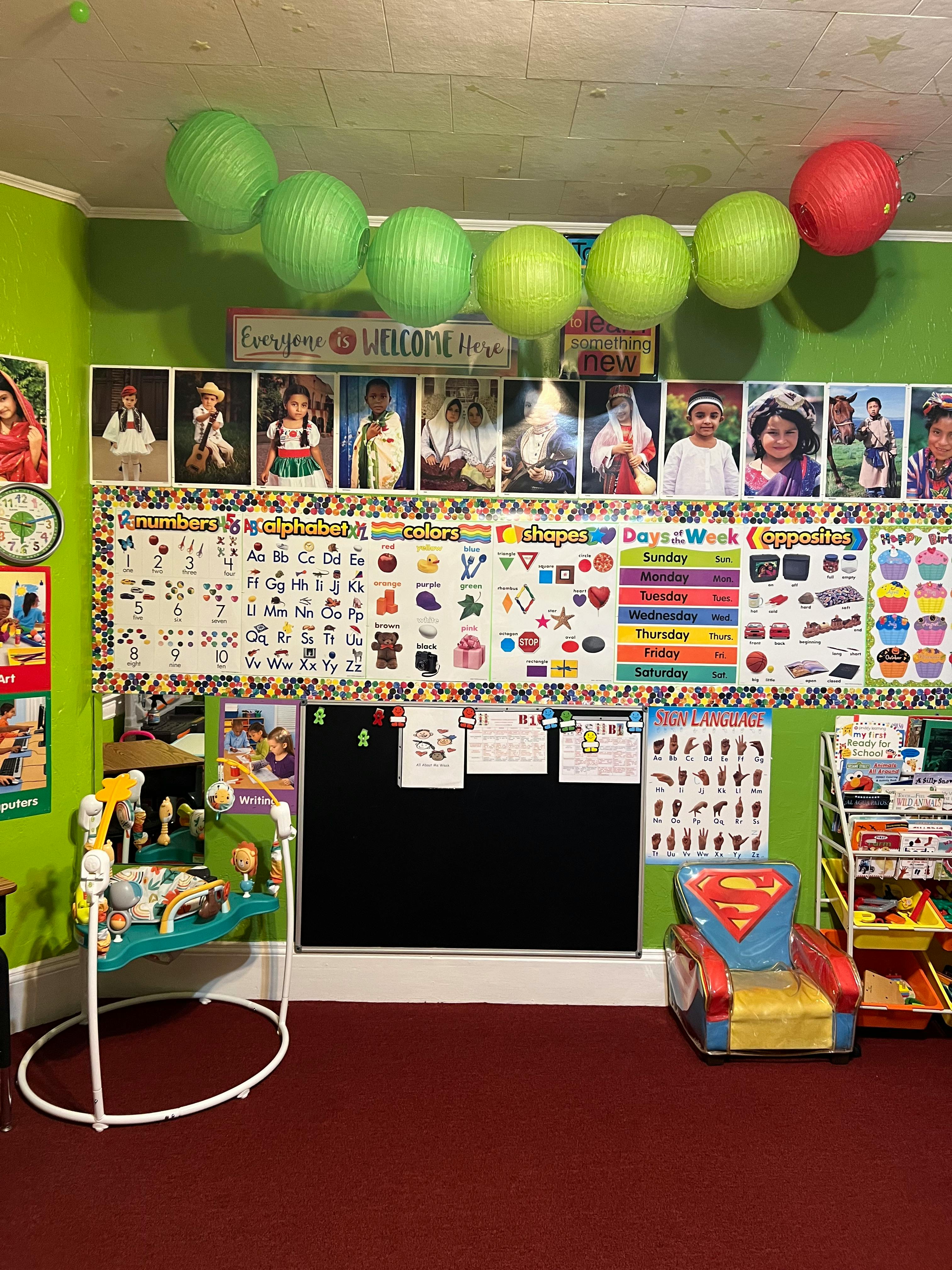Classroom with learning charts, photos, a baby bouncer, and a child's chair