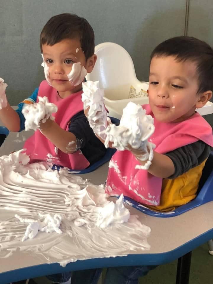 Two children playing with shaving cream at a table