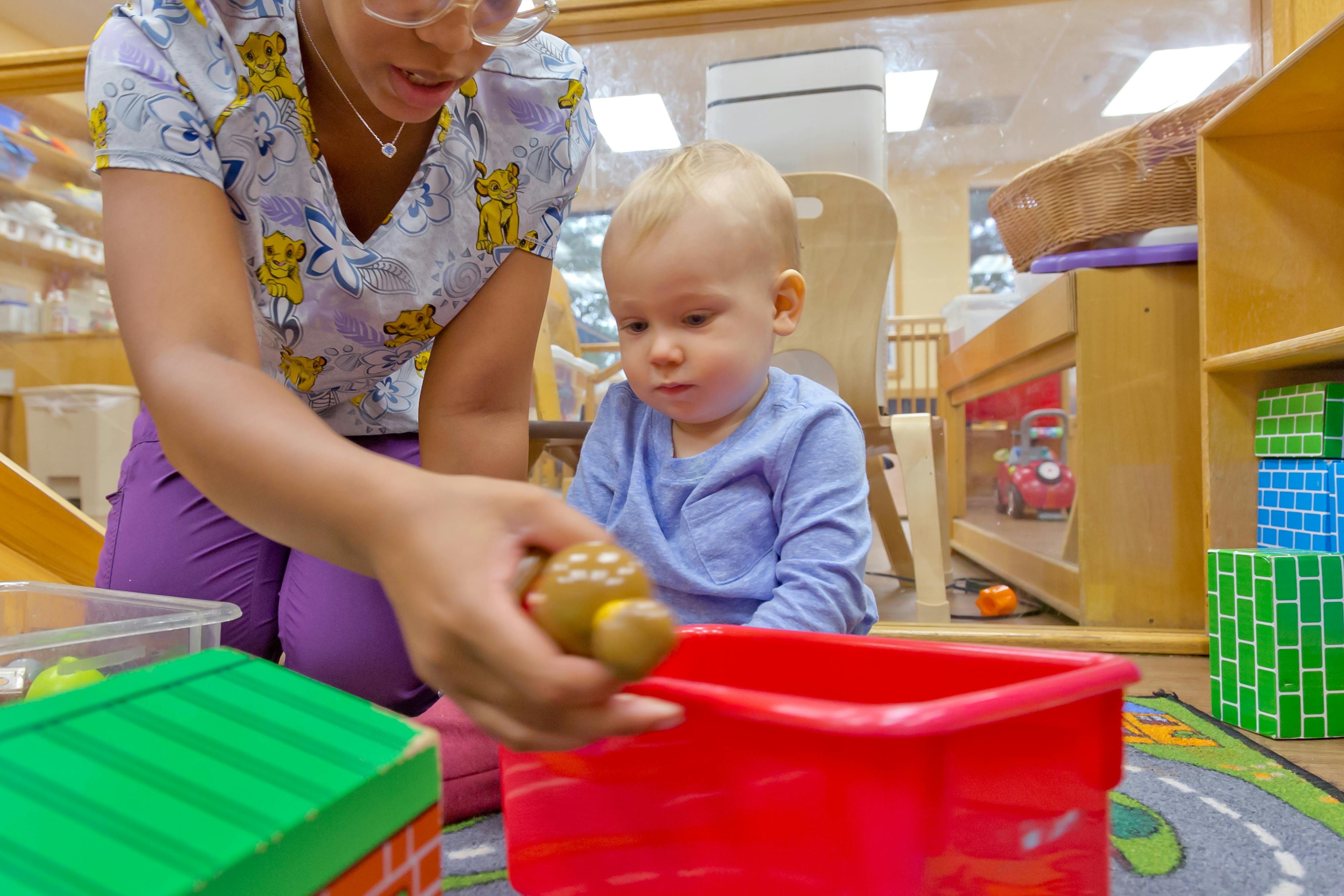 Person holding a toy over a red bin with a child watching