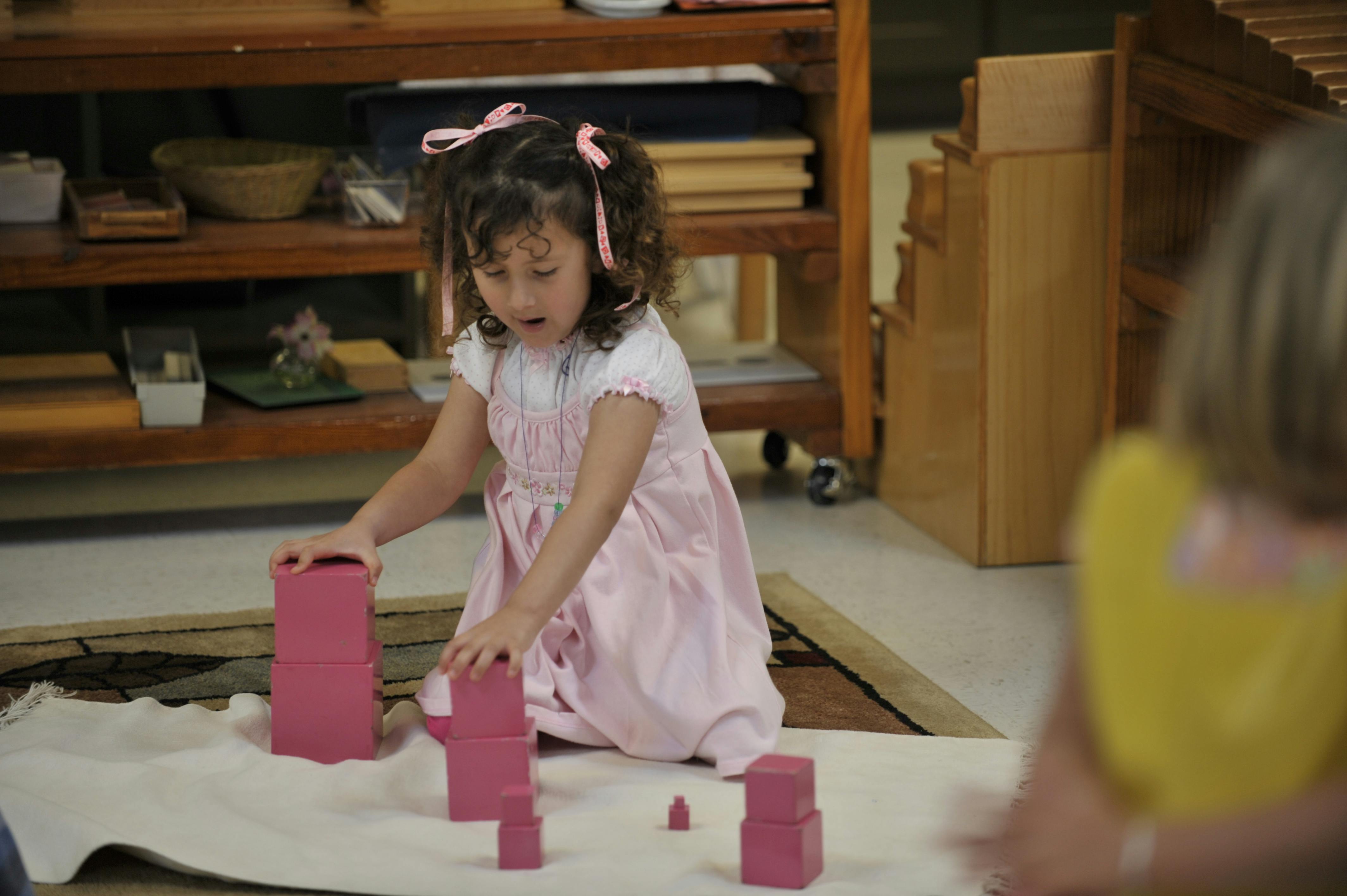 Child kneeling and stacking pink blocks