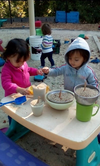 Two children playing with sand and containers at a table