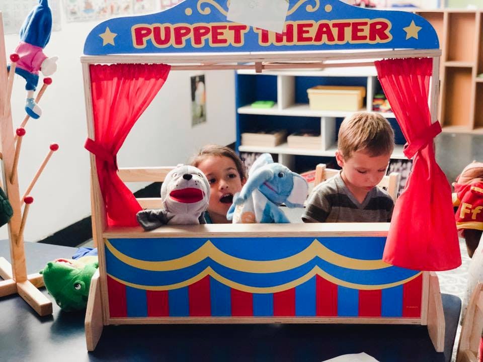 Two children playing with puppets in a puppet theater