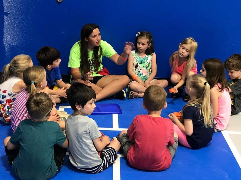 Adult person speaking to a group of children sitting on the floor