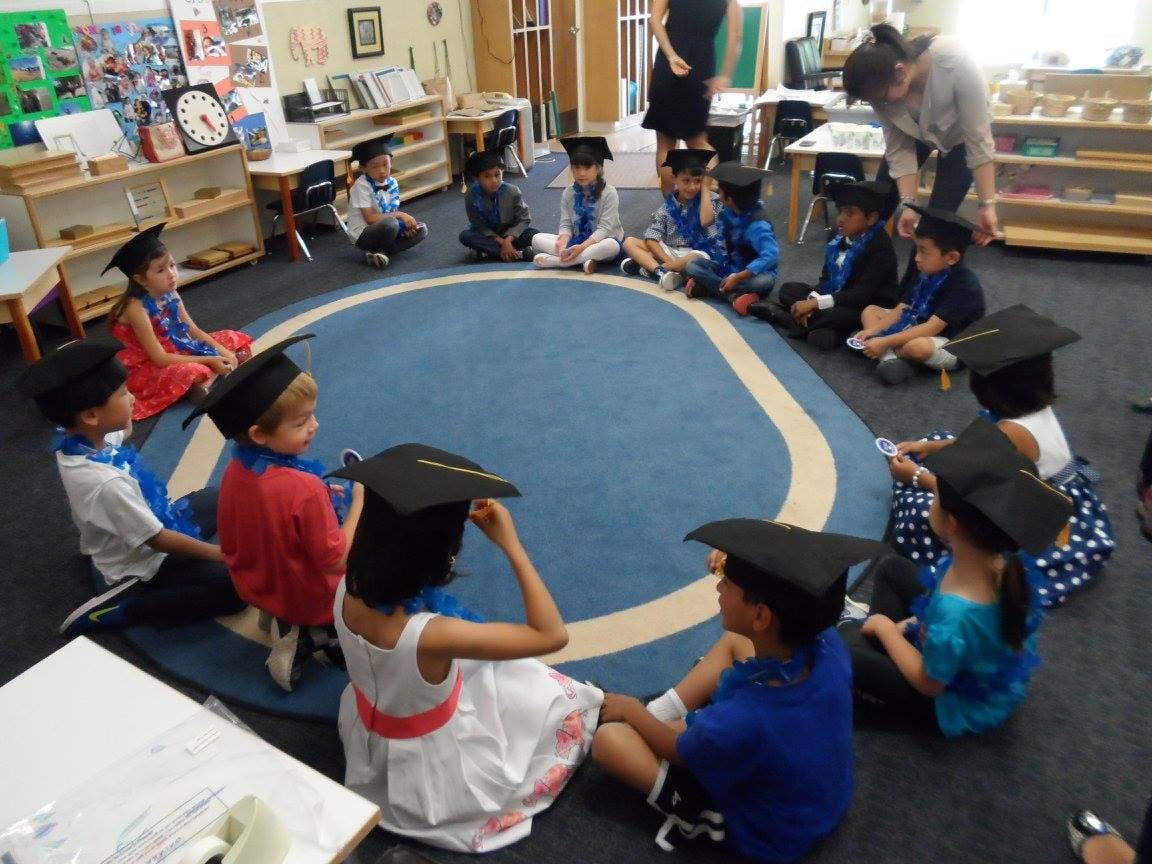 Children wearing graduation caps sitting in a circle on a blue rug