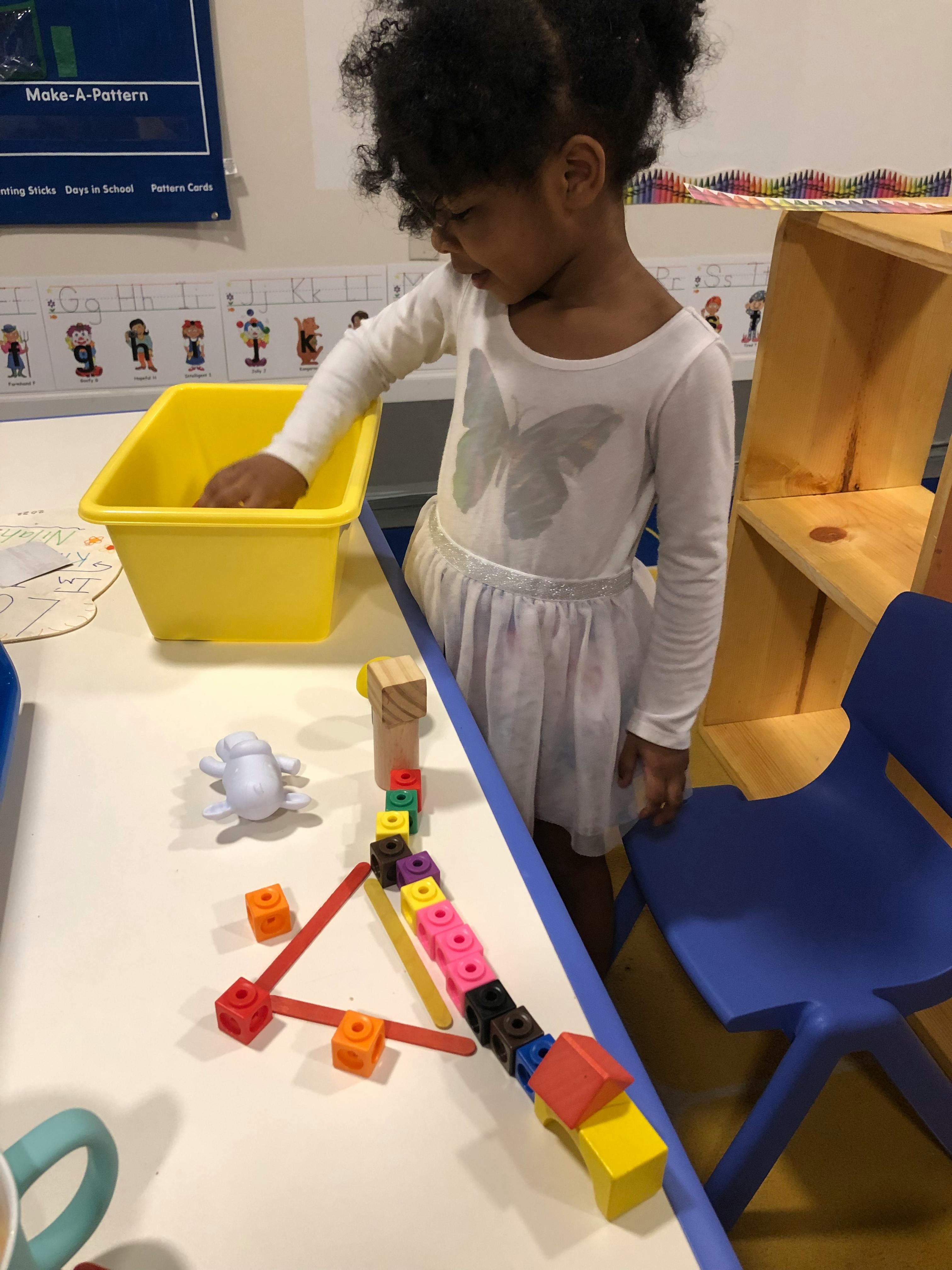Child playing with colorful blocks and a yellow bin at a table