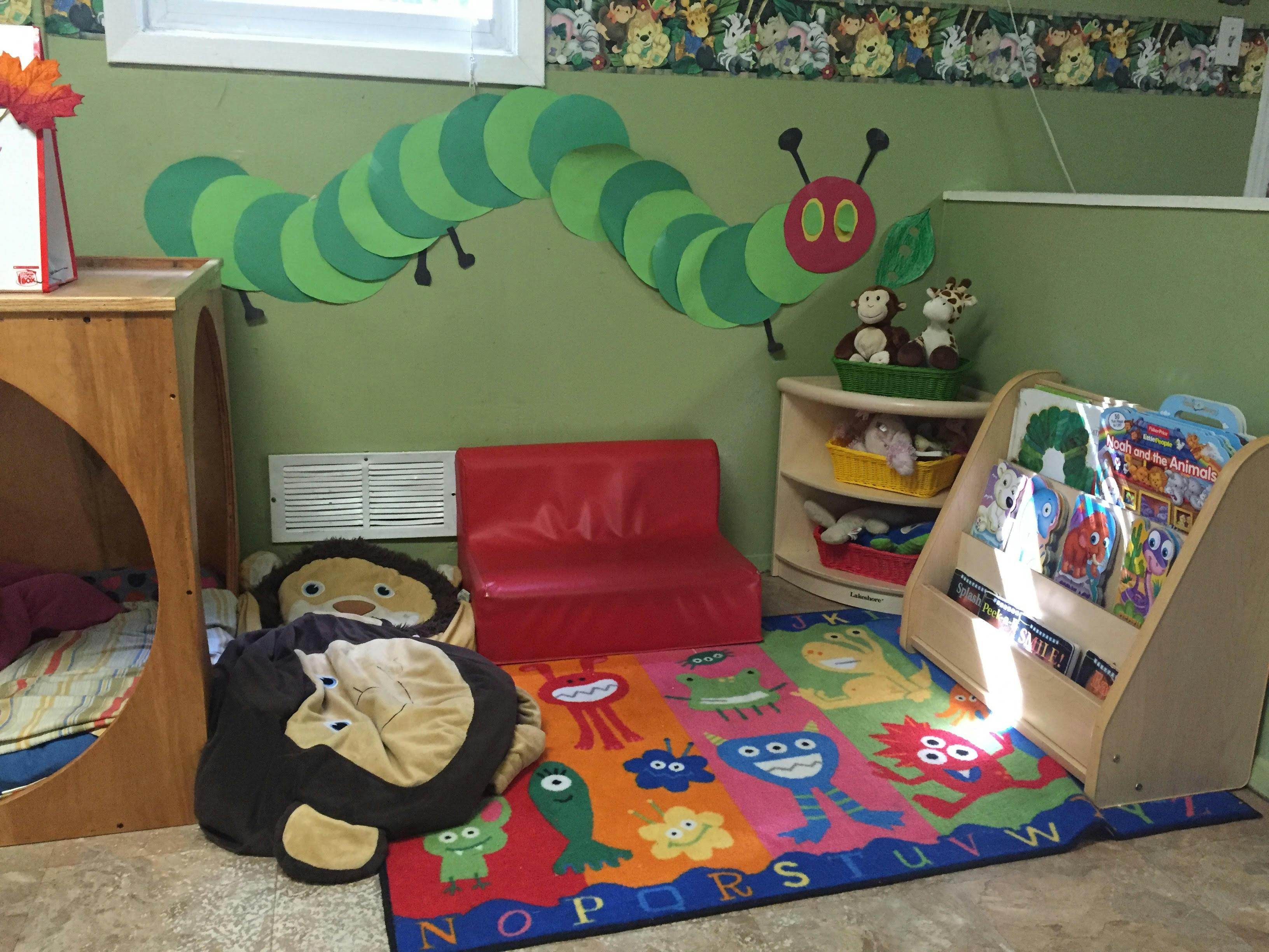 Children's play area with a colorful rug, small red couch, and book display