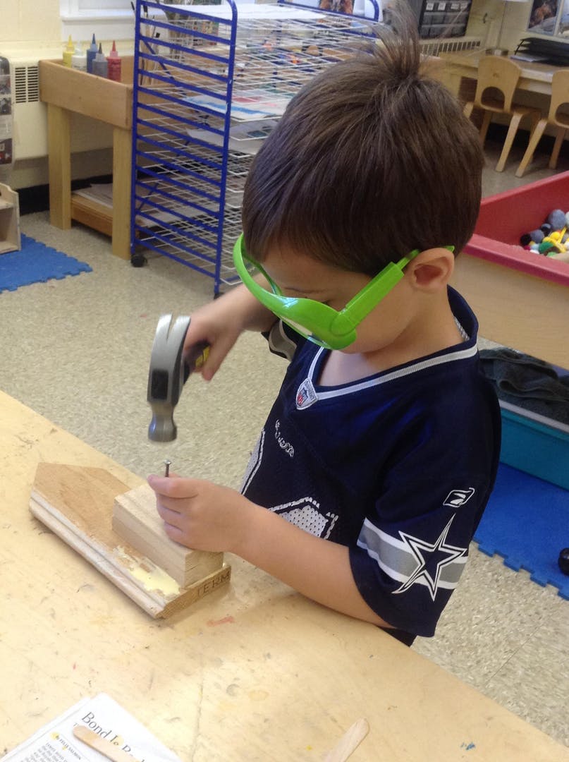 Child in green safety glasses hammering a nail into wood
