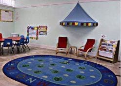 Empty classroom with small tables and chairs, a blue rug, and a canopy
