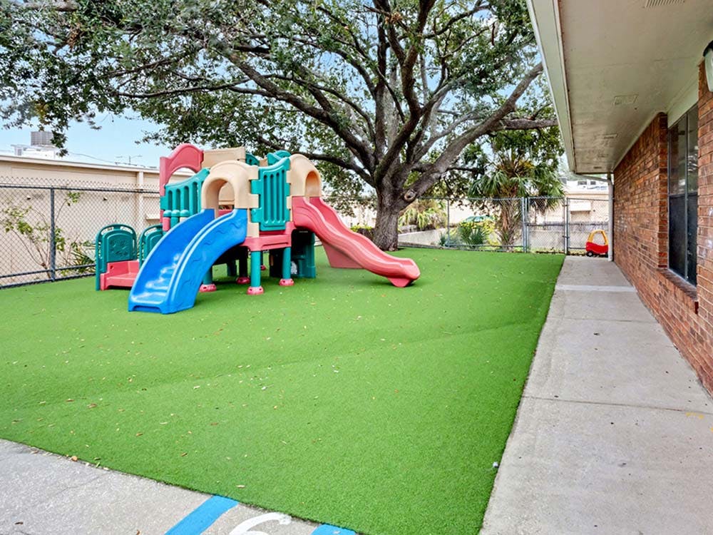 Colorful playground structure with slides on artificial turf next to a building