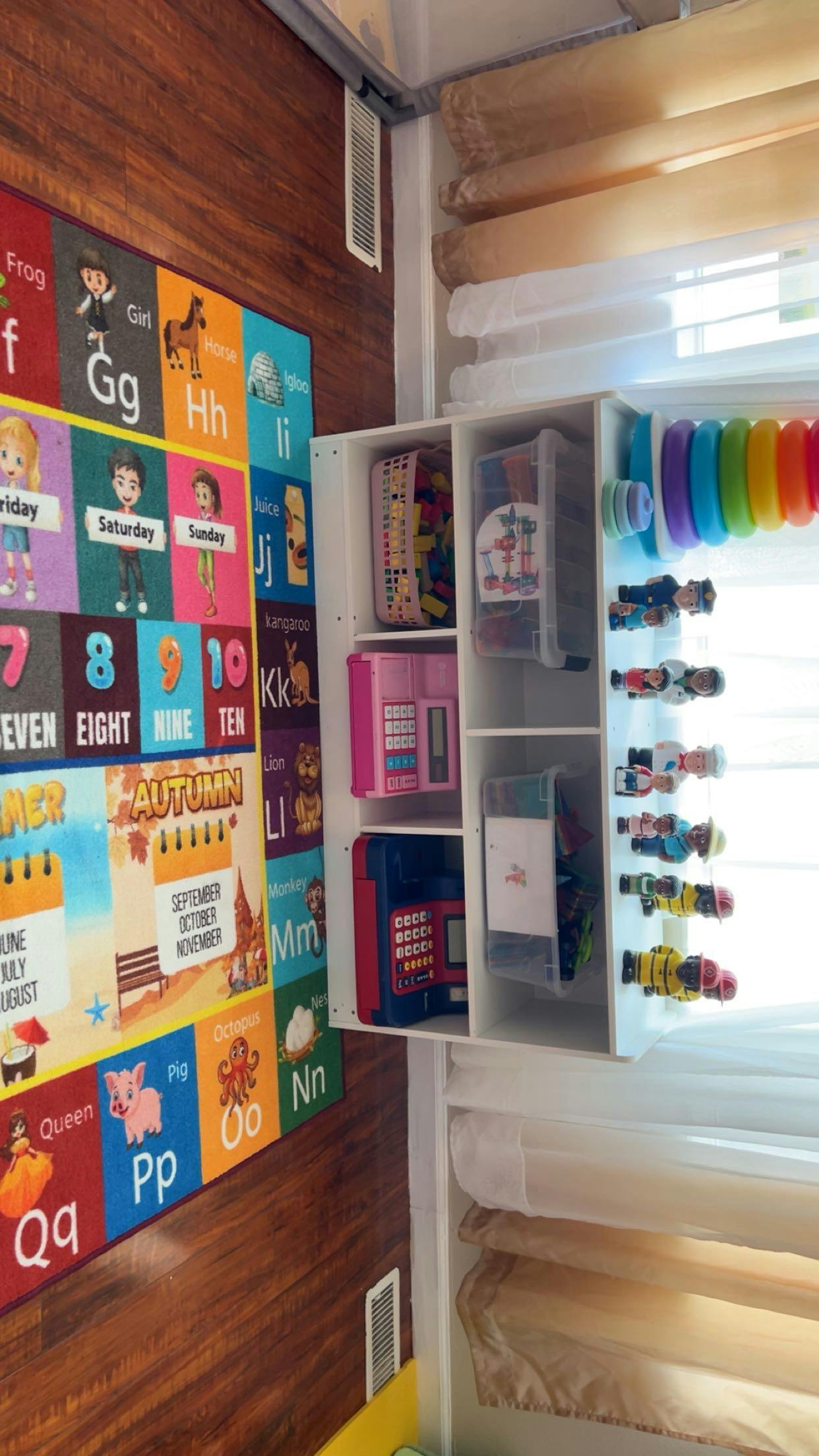Educational floor rug with letters and numbers next to a toy shelf