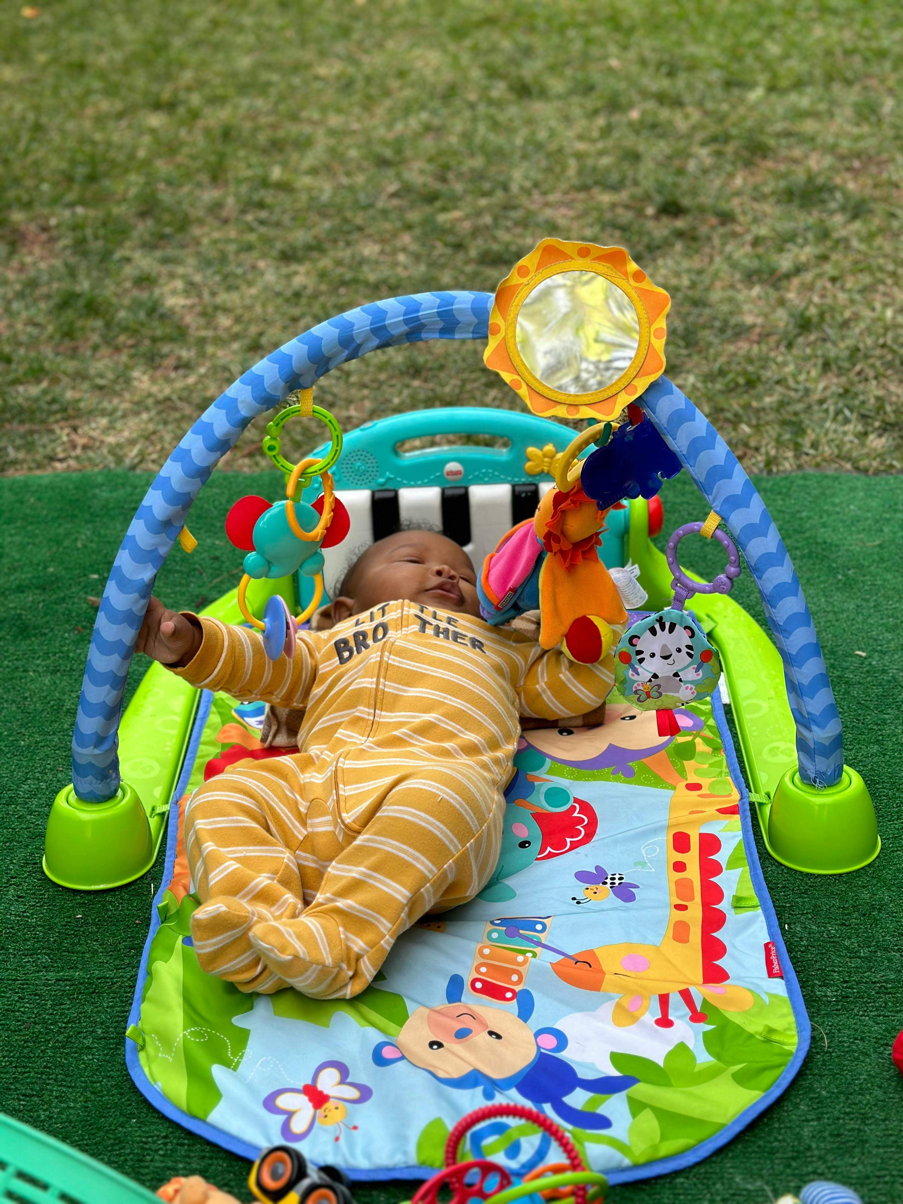 Child in a striped onesie lying on a play mat with toys