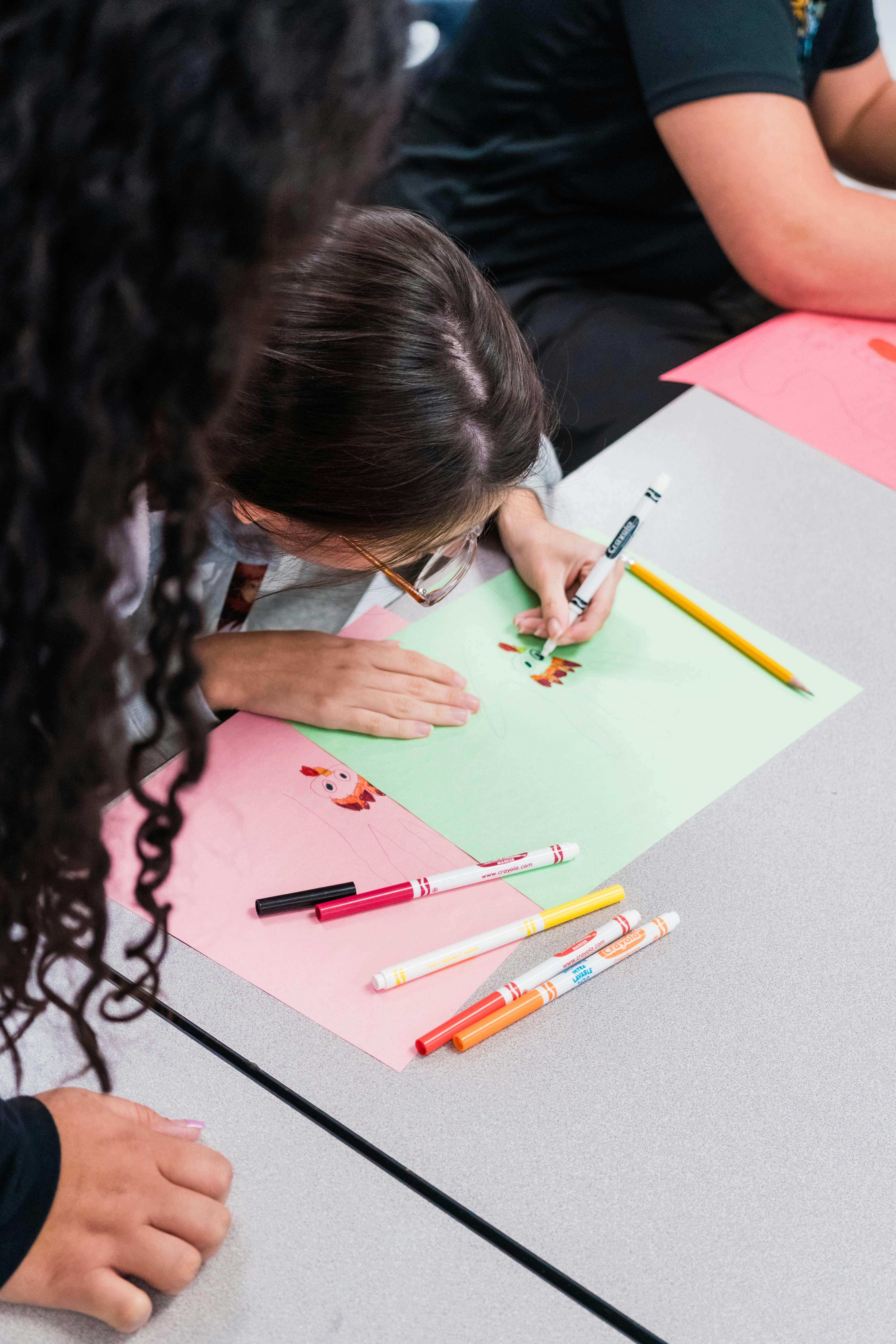 People drawing with markers on colorful paper at a table