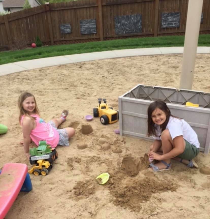 Two children playing in a sandbox with toys