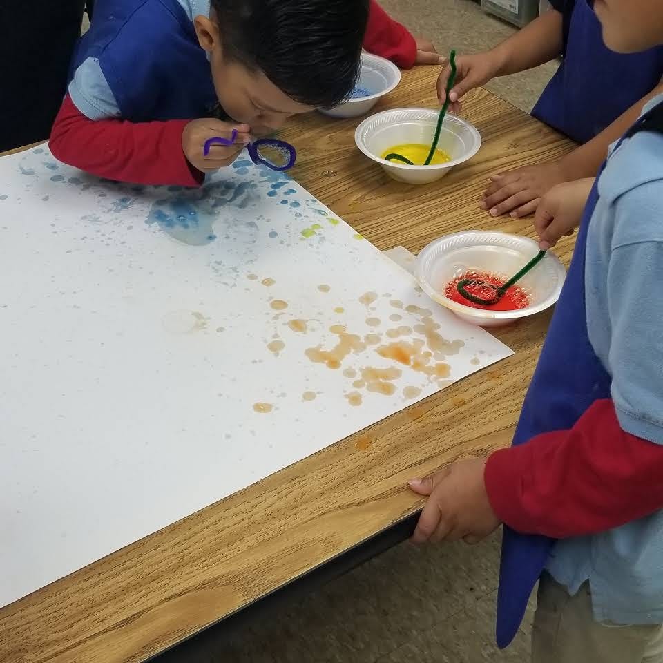 Child blowing paint through a straw onto paper