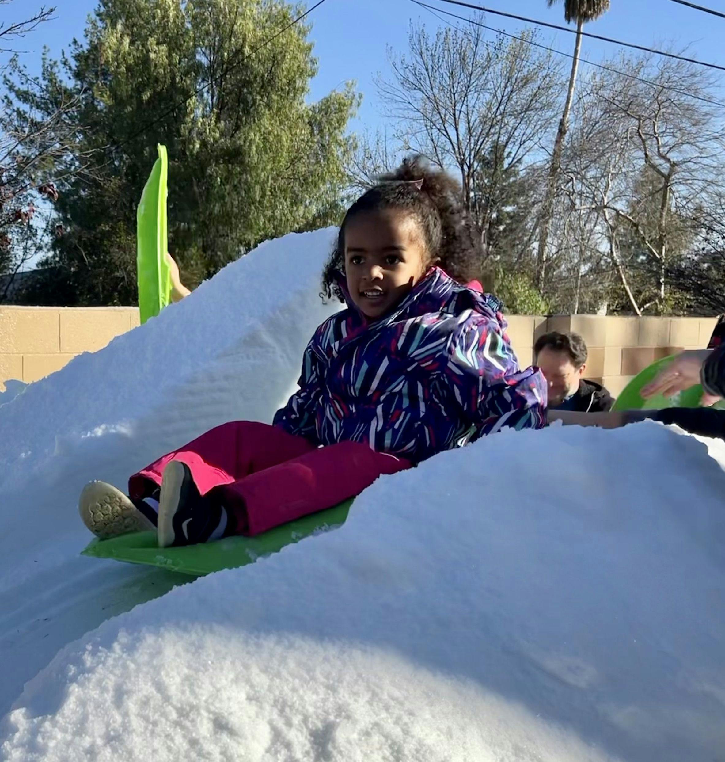 Child sitting on a green sled in snow