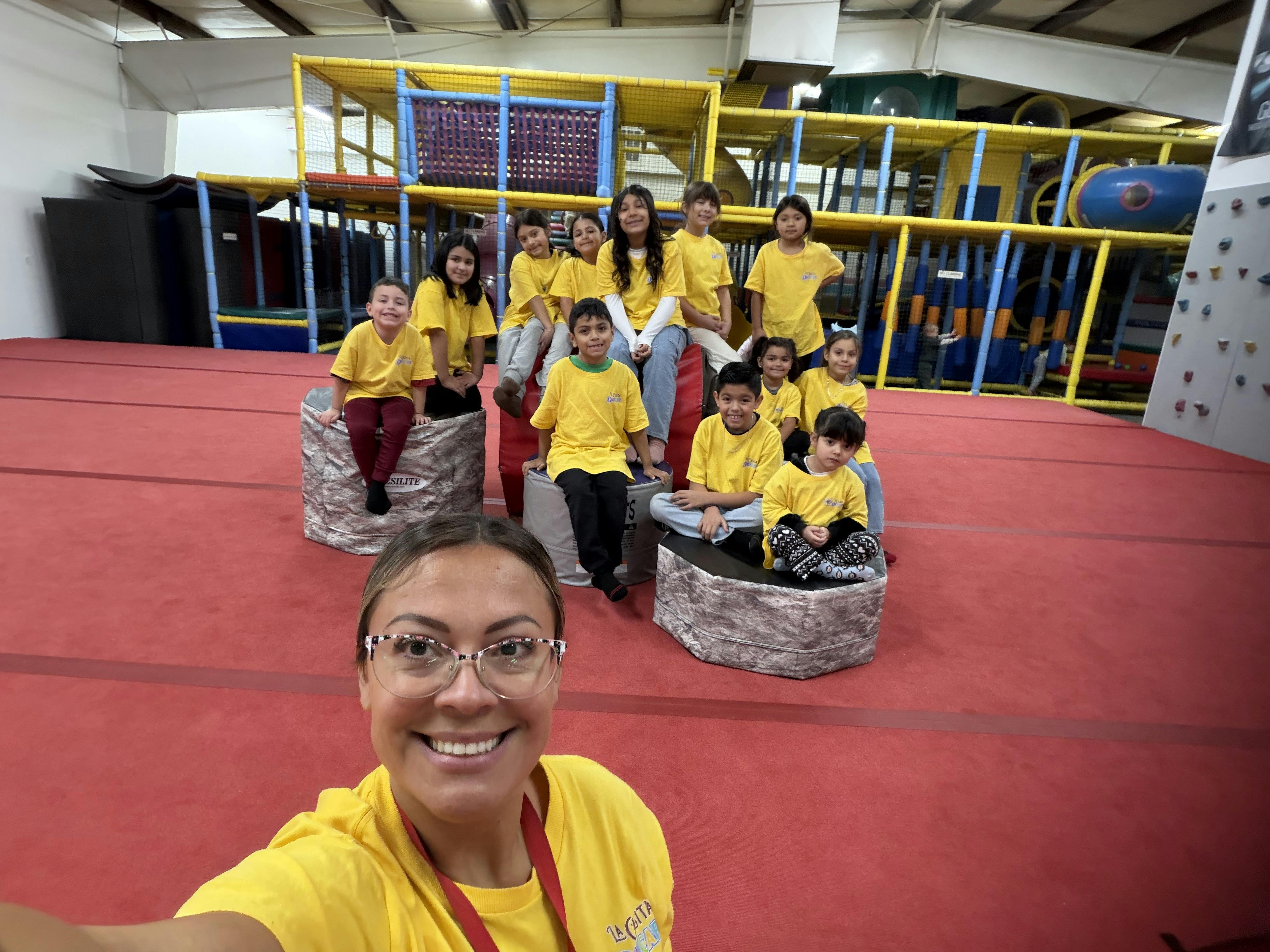 Person in glasses taking a selfie with a group of children behind them