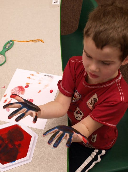 Child with paint on hands over paper and paint tray