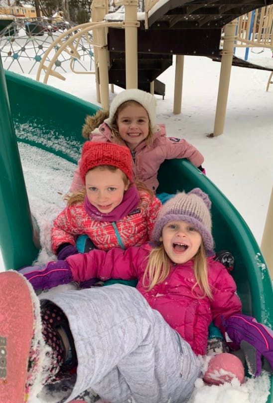 Three children on a playground slide in the snow