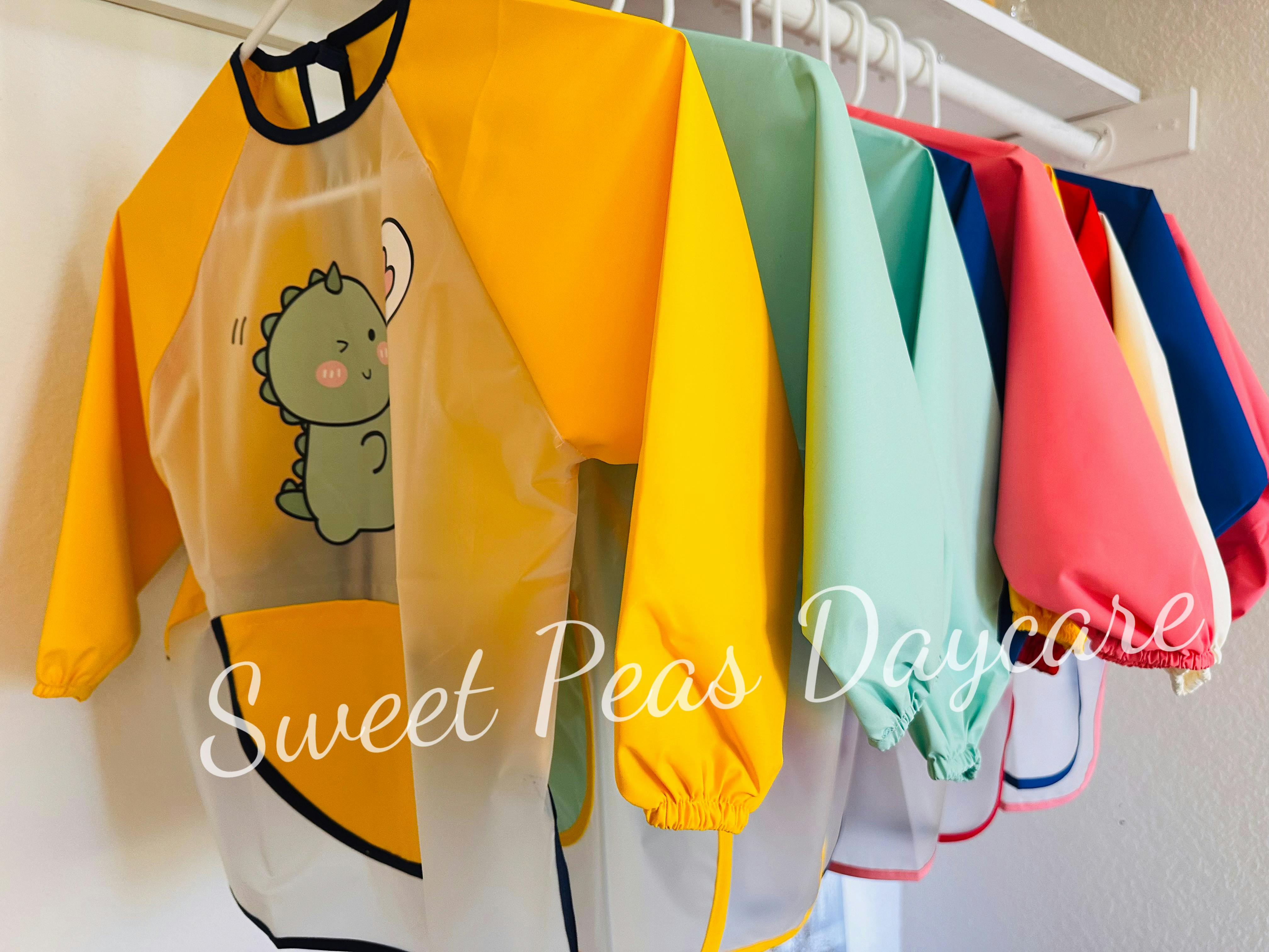 Row of colorful long-sleeved smocks with one featuring a dinosaur