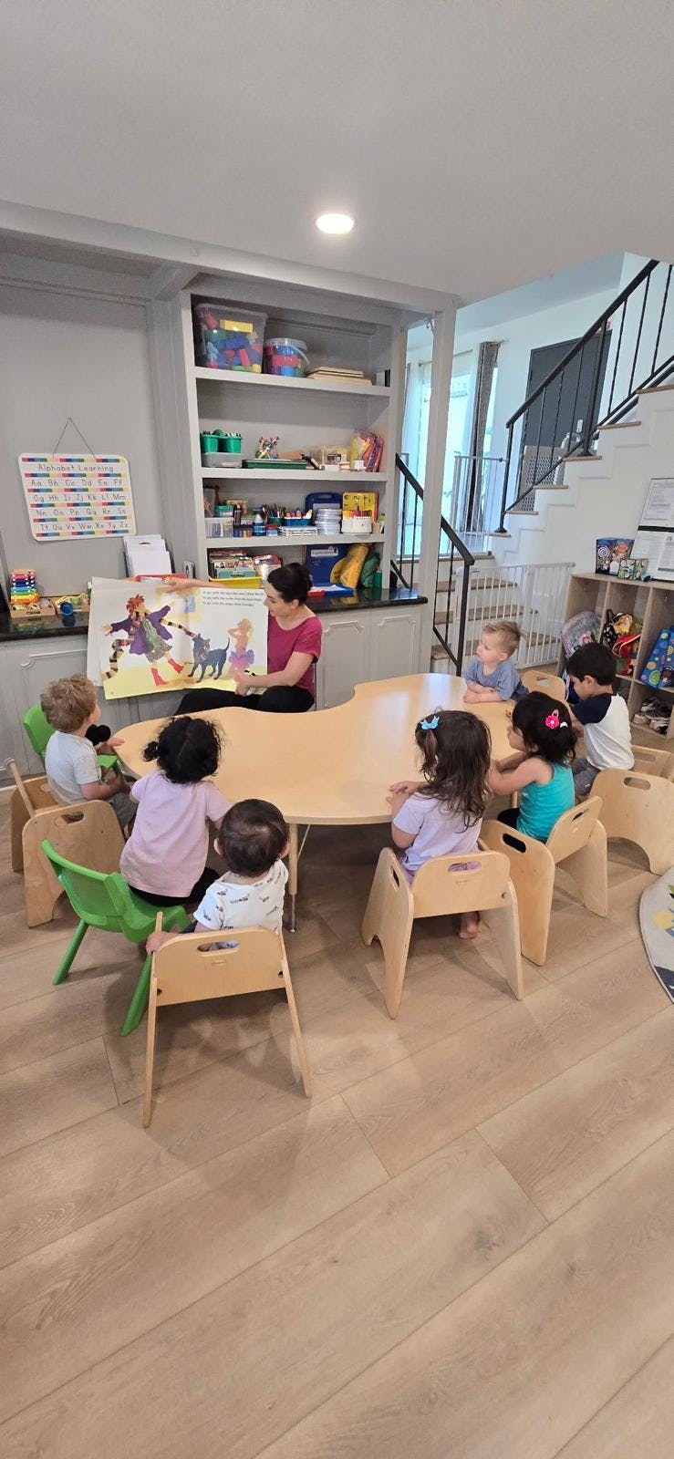 A person reading a book to a group of children seated at a table