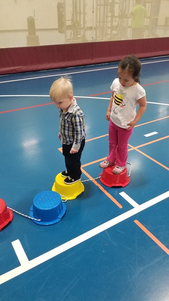 Two children standing on colorful walking stilts in a gym